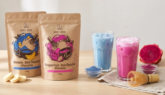 Kolorowa matcha Mary Rose: opakowania blue i pink matcha obok niebieskiego i różowego latte z lodem oraz pitai.